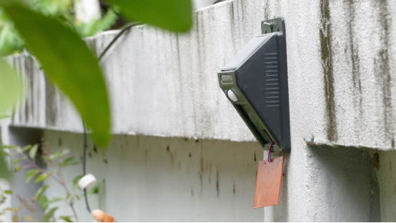 A dual-power outdoor wall light mounted on a concrete wall, featuring a sensor and backup power component, illustrating its reliable, uninterrupted operation.