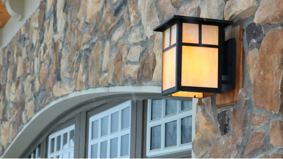 A craftsman-style outdoor wall light mounted on a stone facade, exemplifying the ideal size and proportion for a residential exterior as outlined in architectural guidelines.